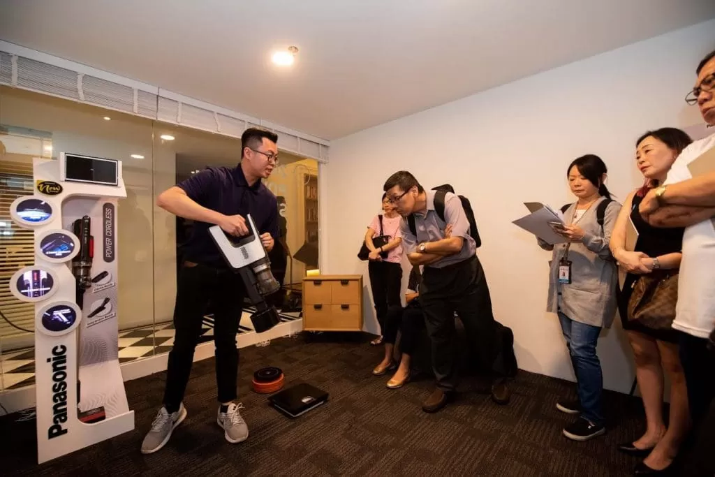 A man demonstrating a cordless vacuum cleaner to a group of people.