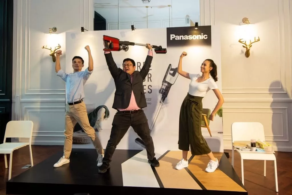 A person holding up a vacuum cleaner with two people posing beside him.