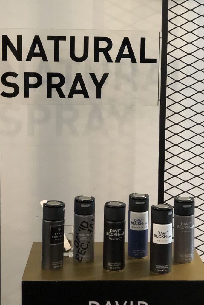 A glass backdrop with the words "natural spray" with David Beckham's different body sprays in front of the glass backdrop on a stand.