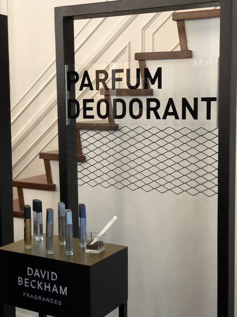 A glass backdrop entitled "Parfum Deodorant" with David Beckham's deodorant lineup on a stand in front of the backdrop.